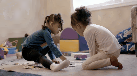 Two children playing together on the carpet. Text reads Encouraging Friendships: Connections with peers are just moments away
